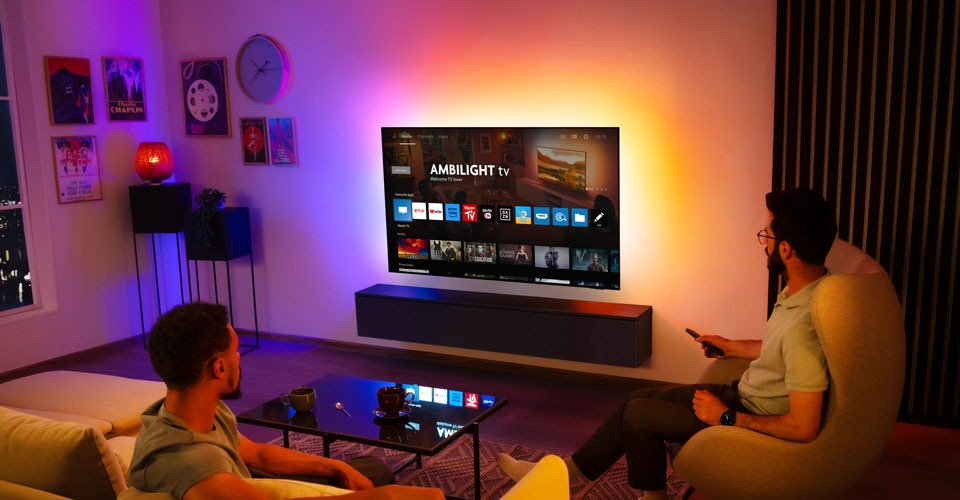 Dvaja muži sledujú nástenný televízor Ambilight v obývačke