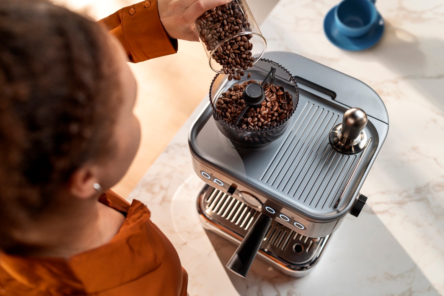 Mladá dáma sype zrnkovú kávu do zásobníka na zrnkovú kávu kávovaru Philips Barista Brew